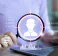 concept of someone looking up another person using a data broker or people search site like USPhoneBook, with a person holding a magnifying glass over digital profile image above a laptop and 