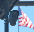 Flock camera monitoring a parking lot as an american flag waves in the background.