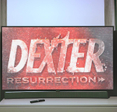 Flat screen TV showing Dexter Resurrection title screen in a dark room with curtains and TV remote on cabinet