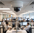 Professional security dome camera installed on office ceiling monitoring open plan workspace with diverse team of employees working at computers in background