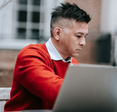 A man in red sitting in front of a laptop.