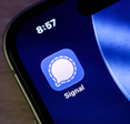Closeup of the signal messaging app icon on a smartphone screen, displaying the iconic white speech bubble logo against a blue background