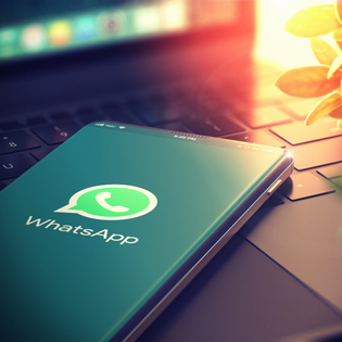 Phone on top of laptop keyboard with Whatsapp logo on the screen