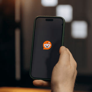 Person holding a phone with the Reddit app loading up on it.