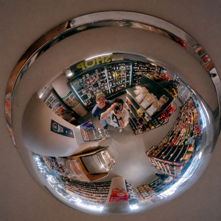 Two people stand under retail surveillance mirror.