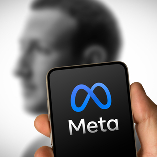 Phone with Meta logo on it in front of faded picture of Mark Zuckerberg.