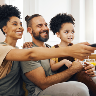 A family of three sits on the couch and watches TV.