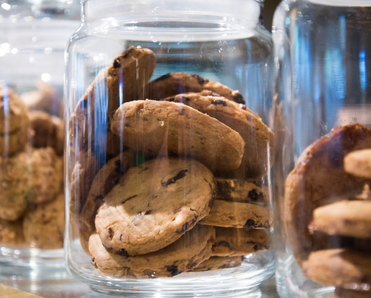 A close up of several chocolate chip cookies in a clear glass jar.