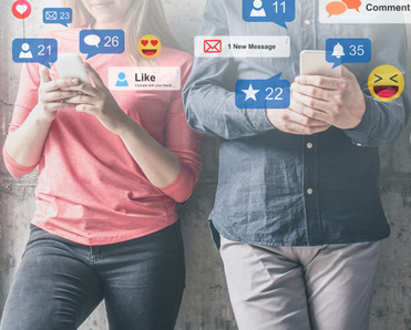 A woman in a pink shirt stands next to a man in a denim shirt as they both scroll through social media on their cell phones while social media notifications pop up around them
