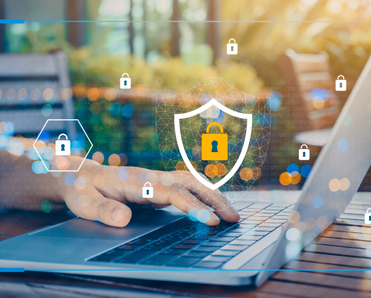 A man&#x27;s hand rests on a laptop keyboard while he sits in an outdoor cafe, lock and shield symbols float in the air