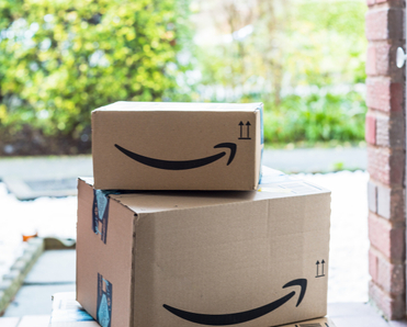 Two brown Amazon boxes with the smile logo sit on a front porch. Amazon brushing scams happen when retailers send you unordered packages in hopes to use your info to boost their sales.