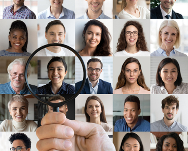 A hand holding a magnifying glass zooms in on a woman&#x27;s profile picture that&#x27;s surrounded by a handful of other men and women&#x27;s profile pics to signify people search.