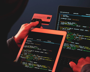 A hooded internet criminal is hacking a laptop in the dark and stealing credit card details.