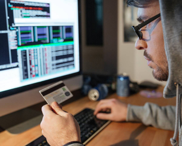 A hooded hacker is stealing money from different credit cards on their computer.