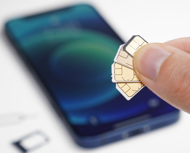 fingers holding several sim cards blurry phone in the back