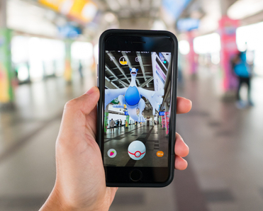 Open public space blurred in the back with hand holding phone screen shows app with game Pokemon GO