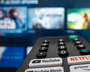 Remote control with button for youtube and other streaming services in the back blurred TV with videos to choose from