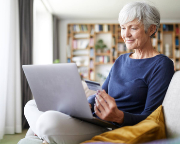 Senior woman using credit card while doing online shopping on laptop at home
