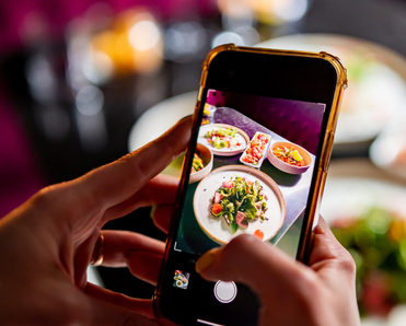 A closeup of a person holding their cell phone to take a photo of food at a restaurant.