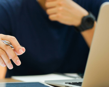Close-up of a man on his Macbook holding a pen in his hand.