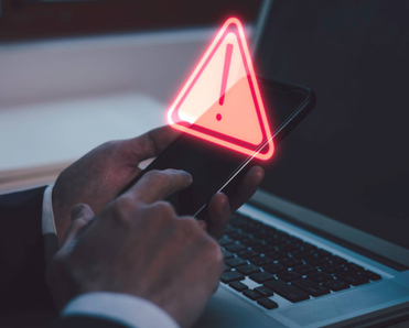 A man holding his smartphone in front of his laptop. There&#x27;s abstract warning above his phone.