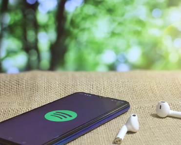 A smartphone displaying the Spotify app next to wireless buds