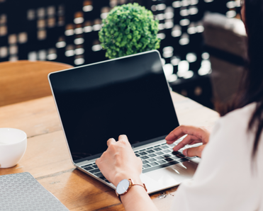 A woman sits at a desk and types on a mac. 