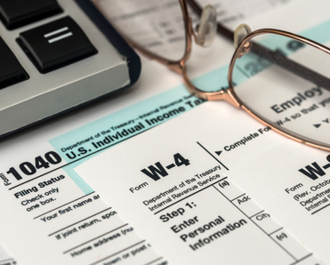 A pair of glasses and the edge of a keyboard are next to a W-4 and a 1040 form. 