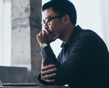 A man sits in front of his computer, resting his chin in his hand.