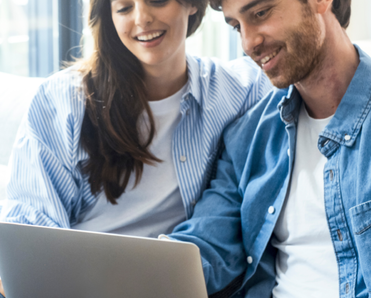 A man and woman sit on the couch while they use a laptop.