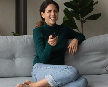 A woman holds a remote while laughing on the couch.