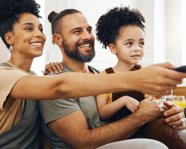A family of three sits on the couch and watches TV.