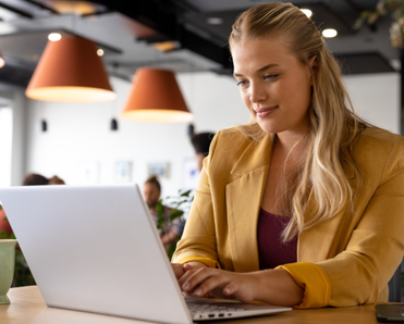 A woman sits at a desk and types on a laptop. 