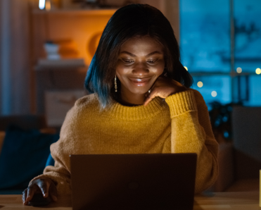 A woman uses her laptop at her table in the evening.