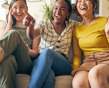 Three friends watch TV and laugh while sitting on the couch.