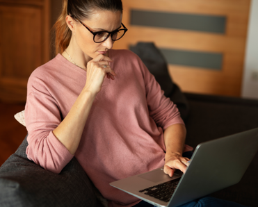 A woman sits on her couch while using her laptop. 