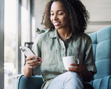 A woman holds a coffee cup and her iPhone.