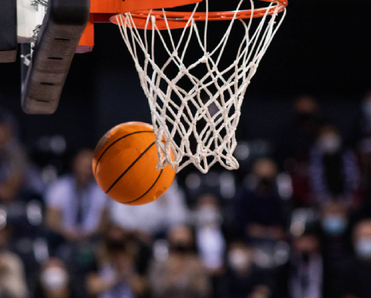 A closeup of a basketball swishing passed the net in a packed stadium