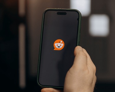 Person holding a phone with the Reddit app loading up on it.
