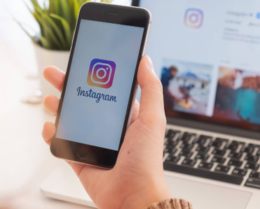 Closeup of woman holding smartphone logged into Instagram in front of laptop