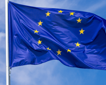 Flag of the European Union waving in the wind on flagpole against the sky with clouds on sunny day.