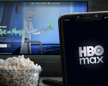 Smartphone displaying HBO Max in front of TV showing Rick and Morty and a bowl of popcorn