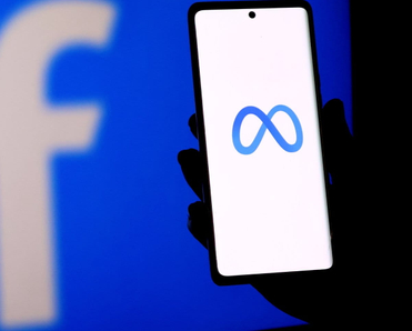 A person holding a smartphone displaying the meta logo in front of a facebook logo screen.