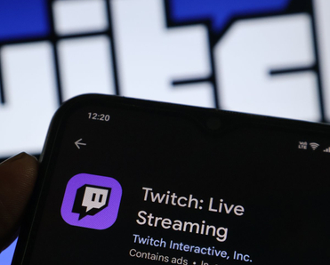 A hand holding a smartphone with the Twitch app open on the screen.