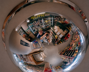 Two people stand under retail surveillance mirror.
