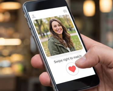Close-up of a hand holding a smartphone displaying a dating app profile with a smiling woman and a 'Swipe right to match' button in a cafe setting.