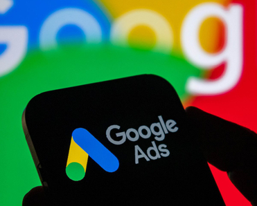 Closeup of a hand holding a smartphone displaying the Google ads logo with the Google logo in the background.