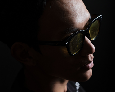 Moody fashion portrait of a man in sunglasses on a dark background.