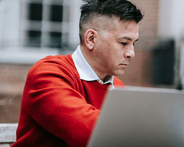 A man in red sitting in front of a laptop.