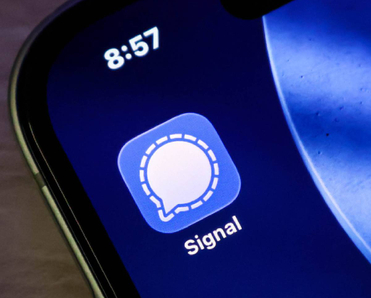 Closeup of the signal messaging app icon on a smartphone screen, displaying the iconic white speech bubble logo against a blue background